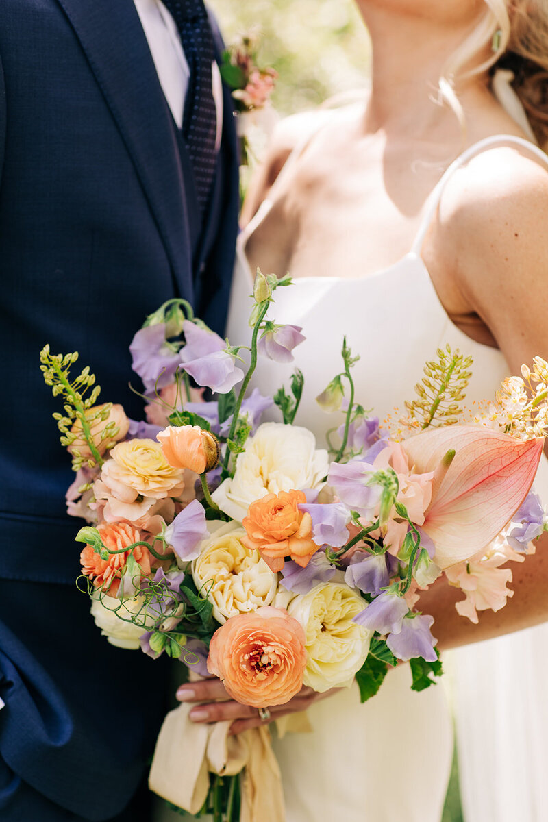 Faceless bride and groom with a colorful bouquet, representing wedding planning by Perfect Thirds & Co in boise. 