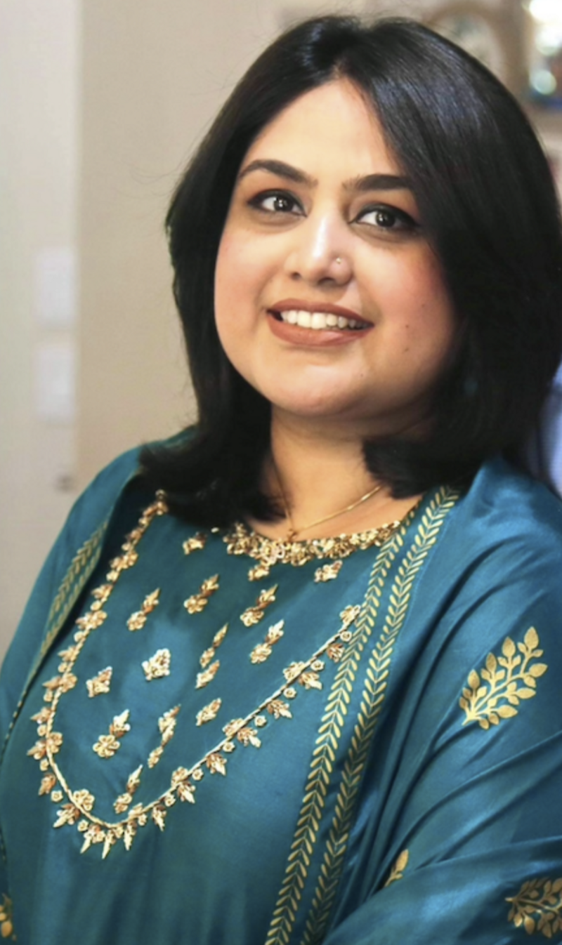 Photo of a woman smiling while wearing a blue sari and has short black hair