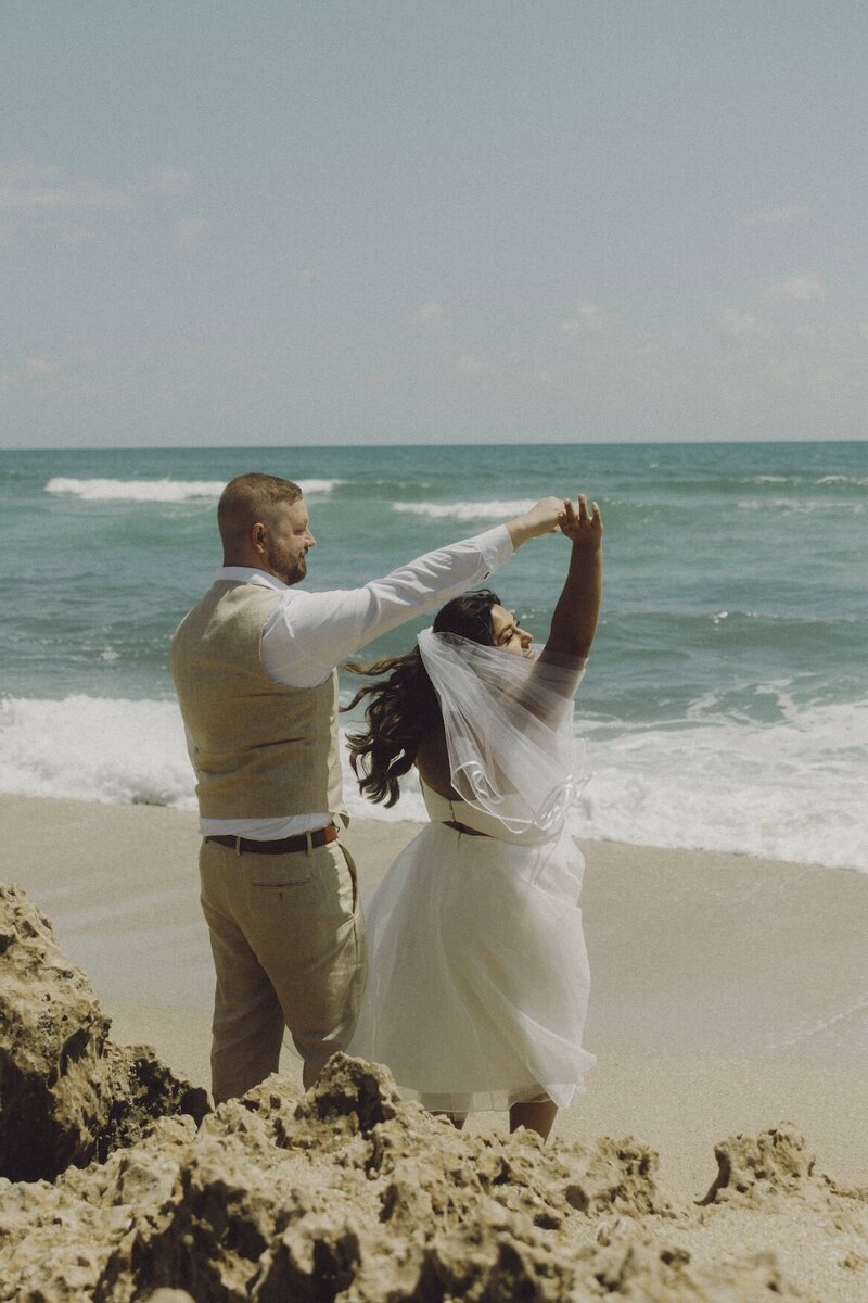 couple holds hands and dances on beach in south florida after wedding ceremony