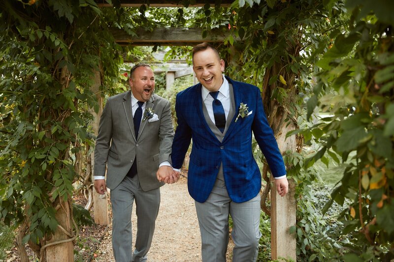 grooms holding hands and walking through a garden
