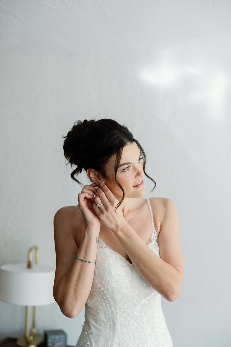 Bride calmly puts on earrings while wearing her wedding dress.