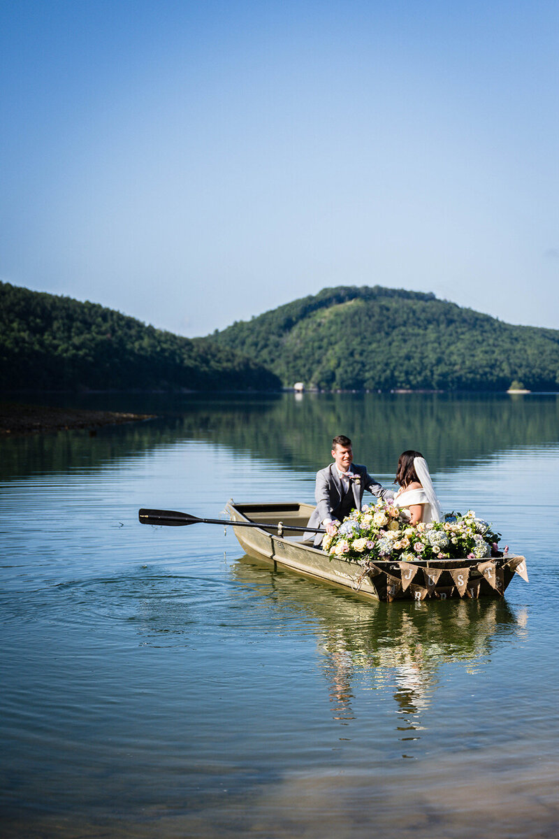 A couple on their elopement day ride around in a rowboat at Carvin's Cove in Roanoke, Virginia. The boat is adorned  with pastel florals and a sign hanging from the back that says "just married."