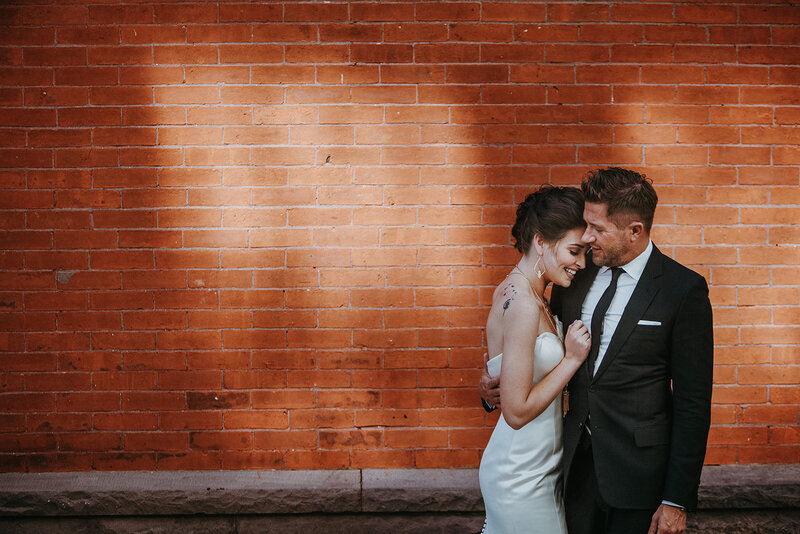 A bride and groom snuggle in front of the brick wall at Market Alley in Lancaster