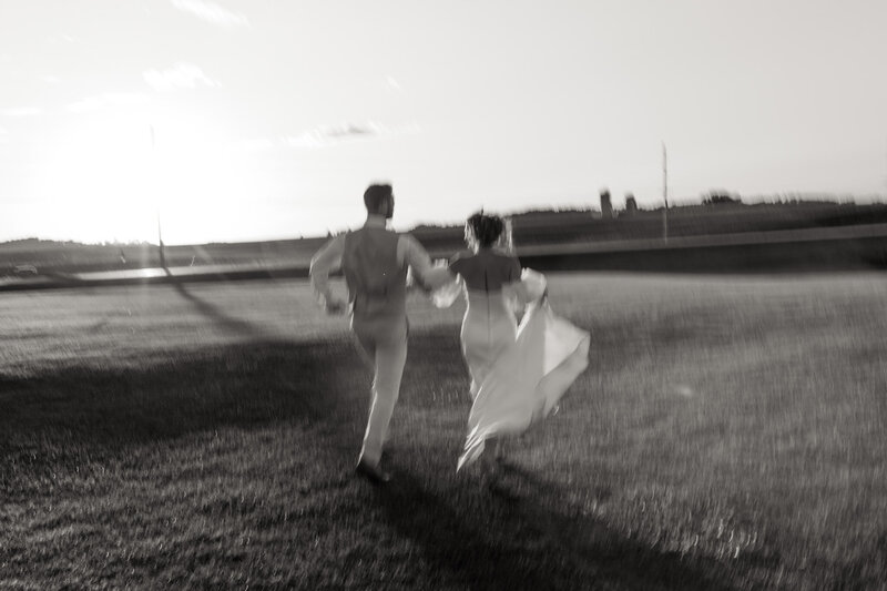 Black and white image of a wedding couple running into the sunset with motion blur taken by a Minnesota and travel elopement photographer