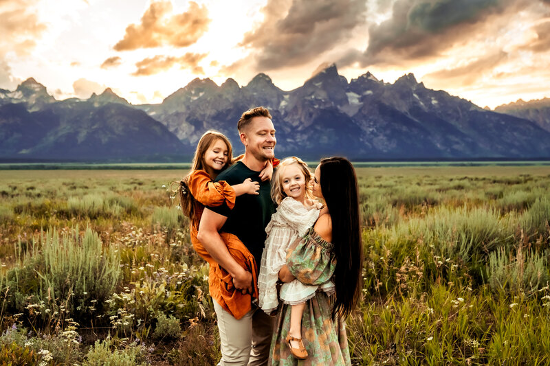 Family Photographer, a young family with two daughters stands before a mountain scape and meadow