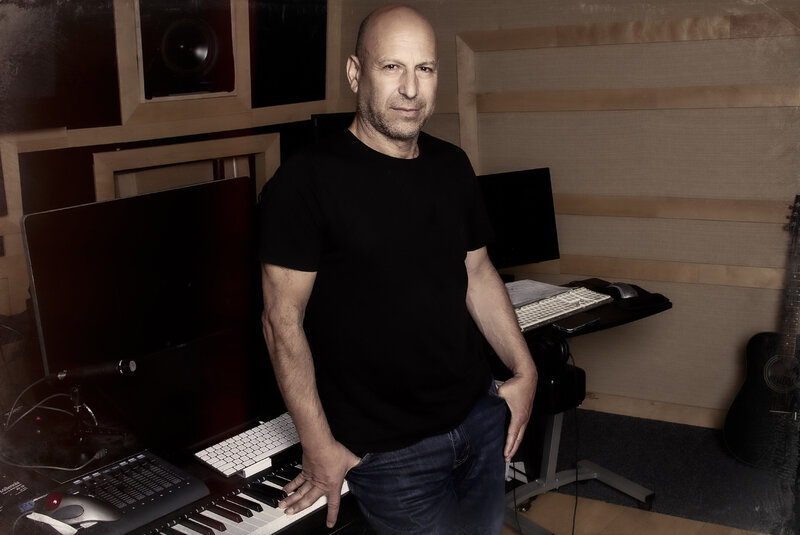 Producer portrait Inon Zur wearing black t shirt leaning against sound board