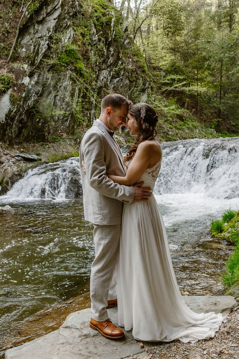 A couple stands head to hand with a small waterfall behind them.