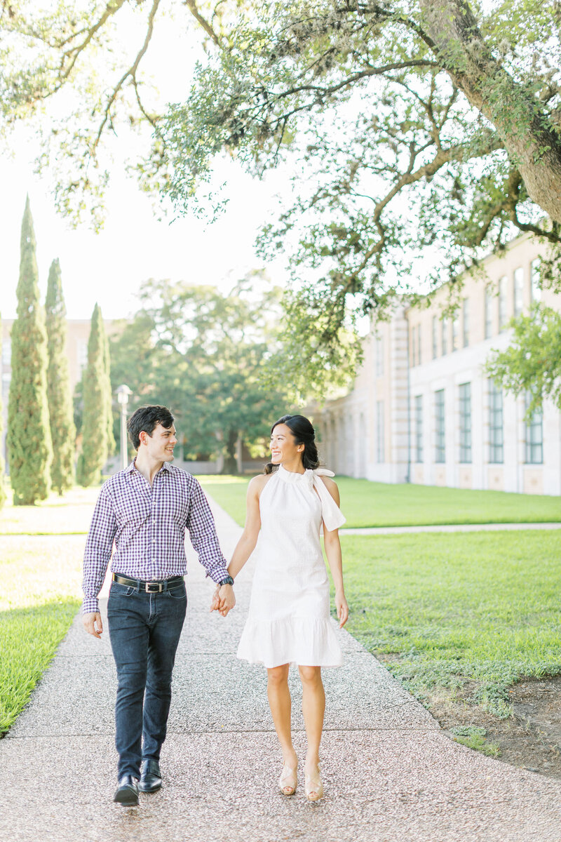 Two people holding hands walking on a paved path at Rice University at sunset.
