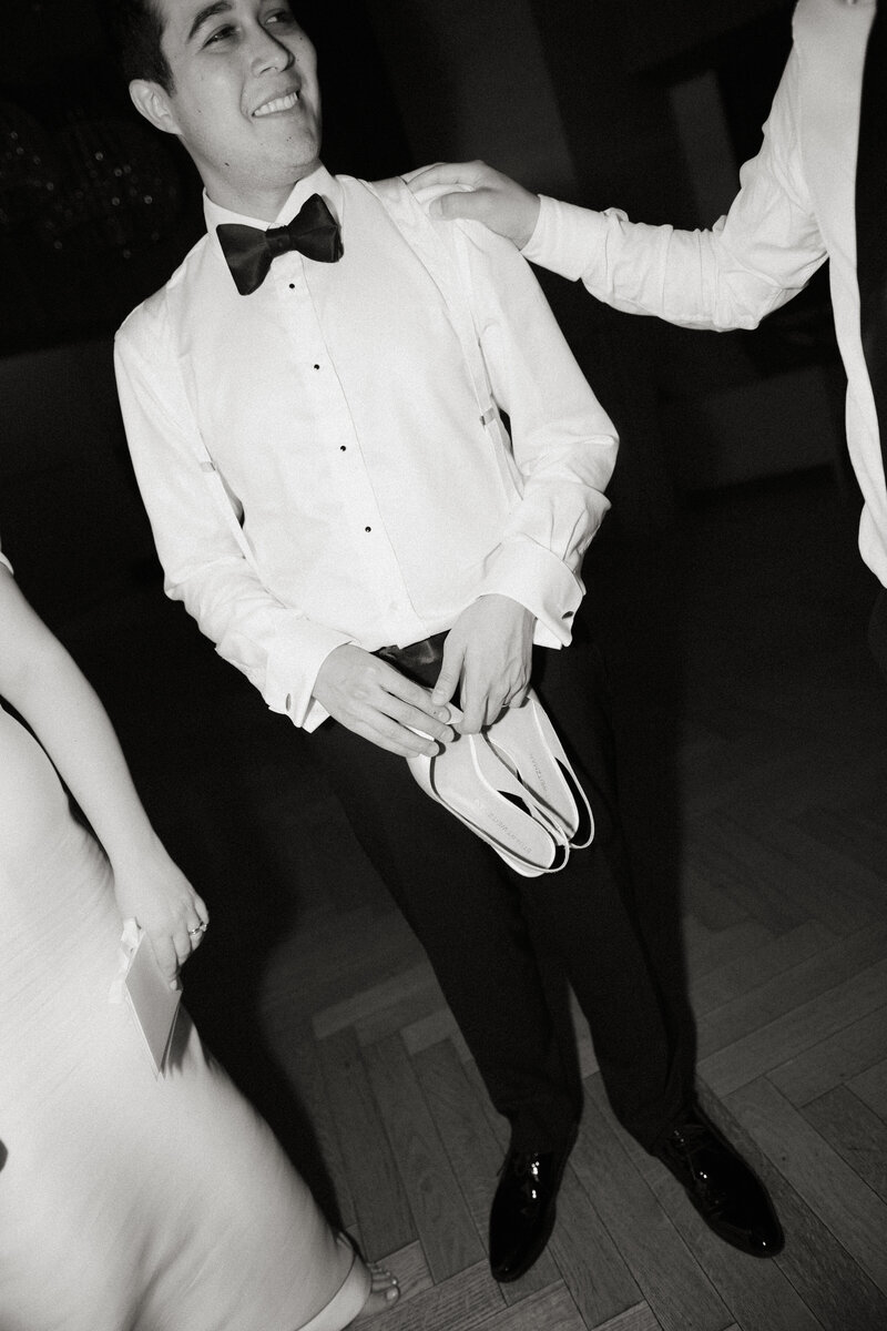 high end flash photography of groom holding designer shoes on wedding night