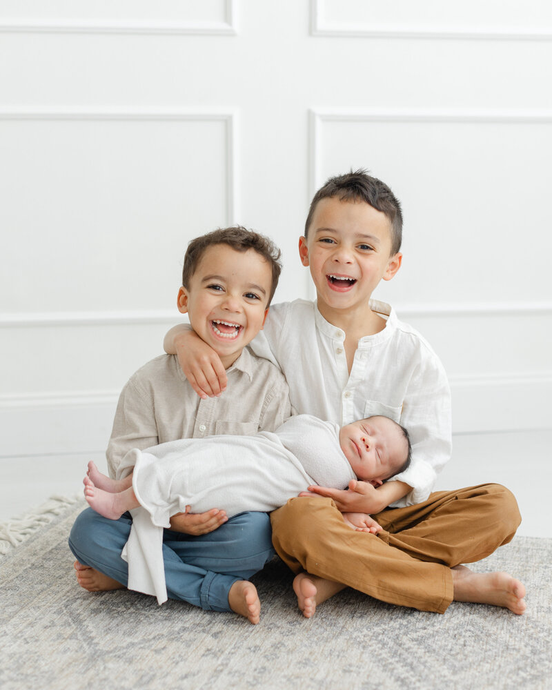 2 young boys smile and hold their newborn baby brother