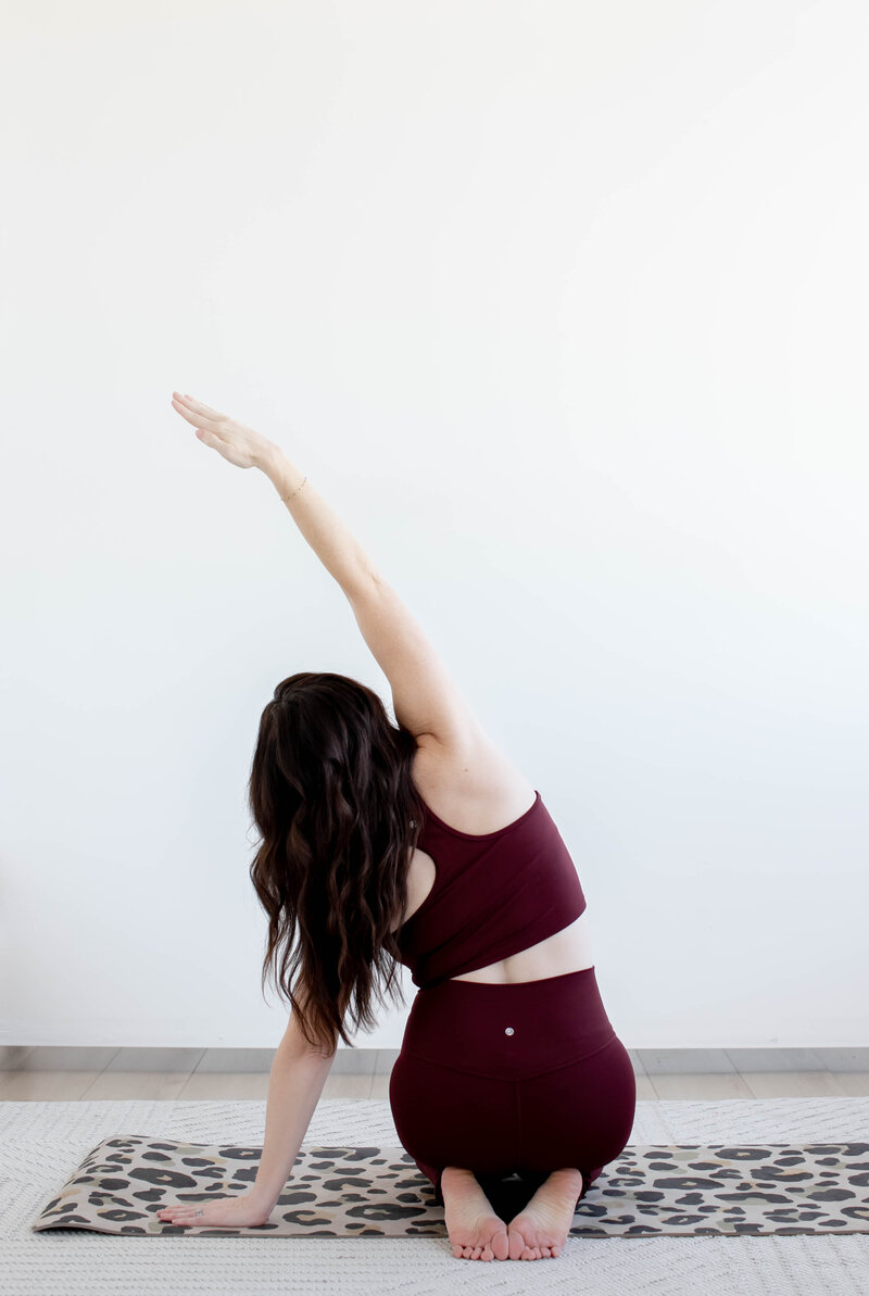 Woman in seated position stretching arm overhead towards left side