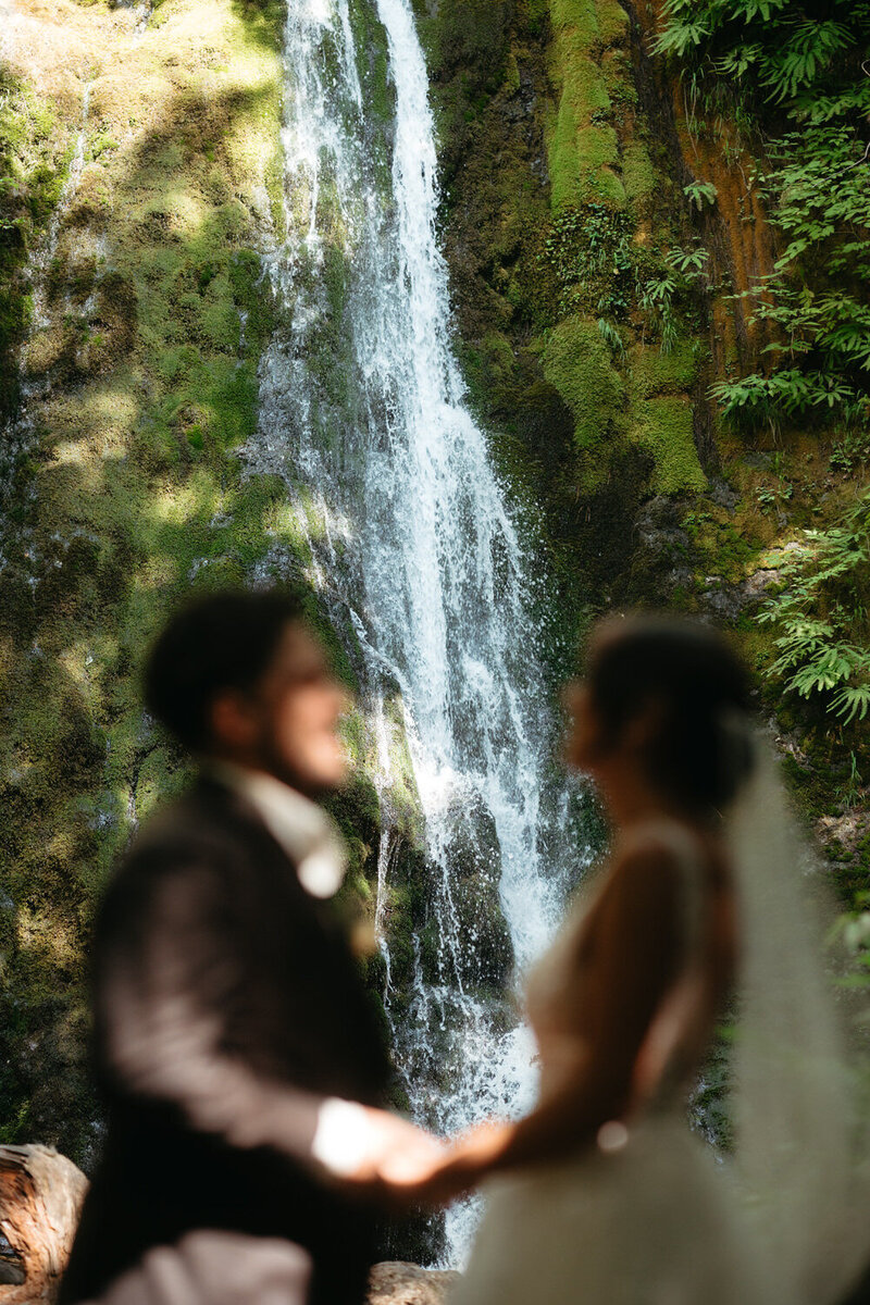Couple holding hands facing each other under Madison Falls in Olympic National Park