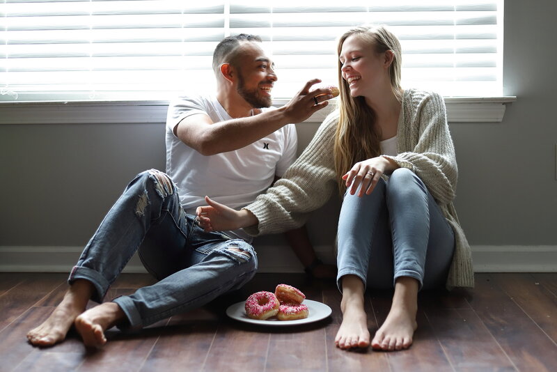 Couple sitting on the floor of their home eating doughnuts and laughing