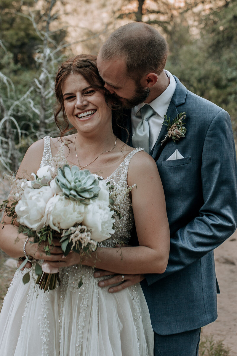 groom kissing bride with white and succulent florals at sedona hiking trailing wedding