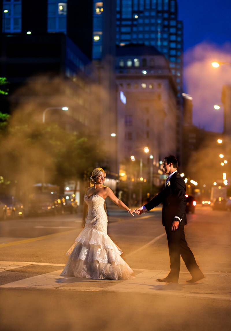 A couple walks through the steam in downtown Cleveland at night just as the sun set.