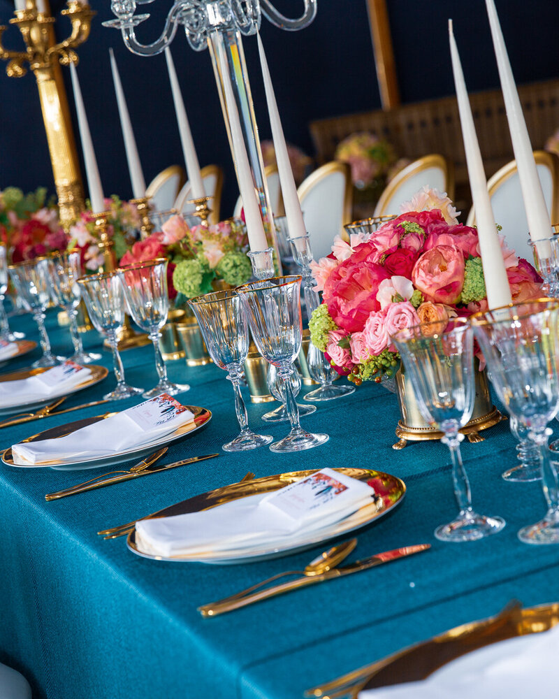 A teal, gold and pink dinner table is set for a party or wedding.