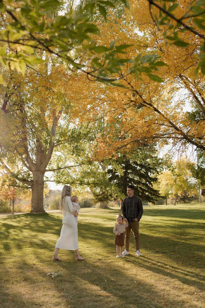 A mom and dad hold their 2 baby girls in a park outside.