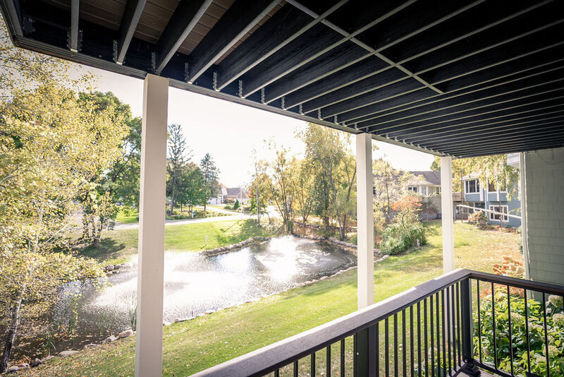 View from lower deck through white upper deck posts and out onto a small wooded pond with fountain. 