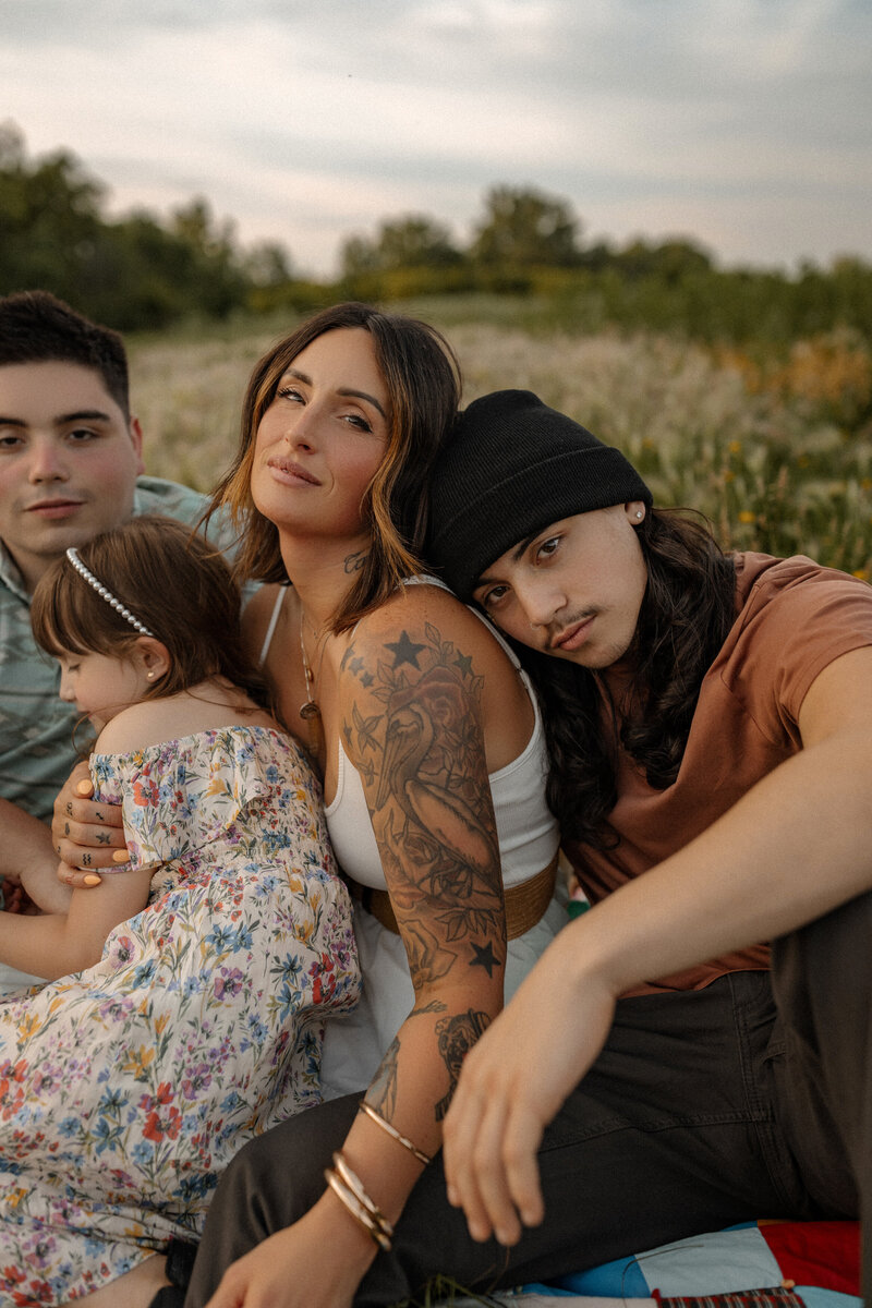Mother holds her young daughter while snuggling her teenage sons in a pretty Ames, IA flower field.