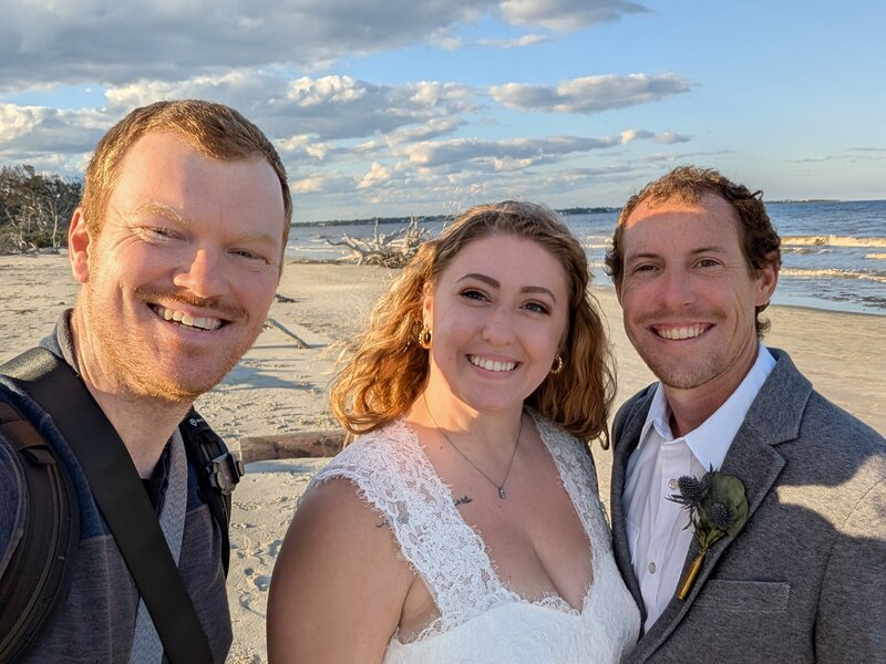 Elopement photographer takes selfie with married couple on the beach