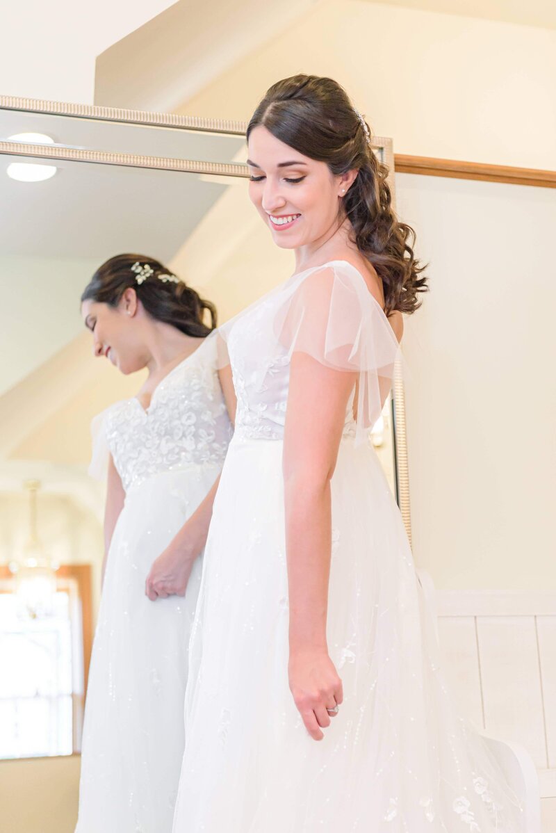 A bride looks down at her dress in front of a mirror.