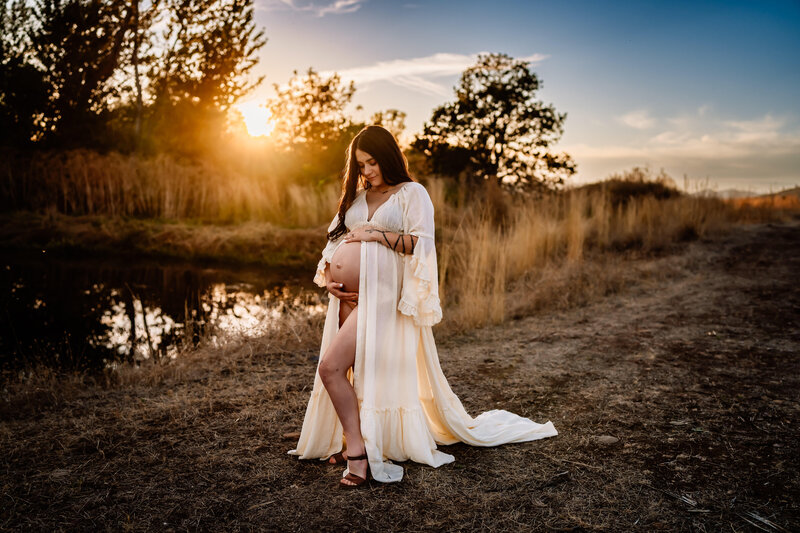 Maternity Photographer, a pregnant woman stands before a country pond at sunset