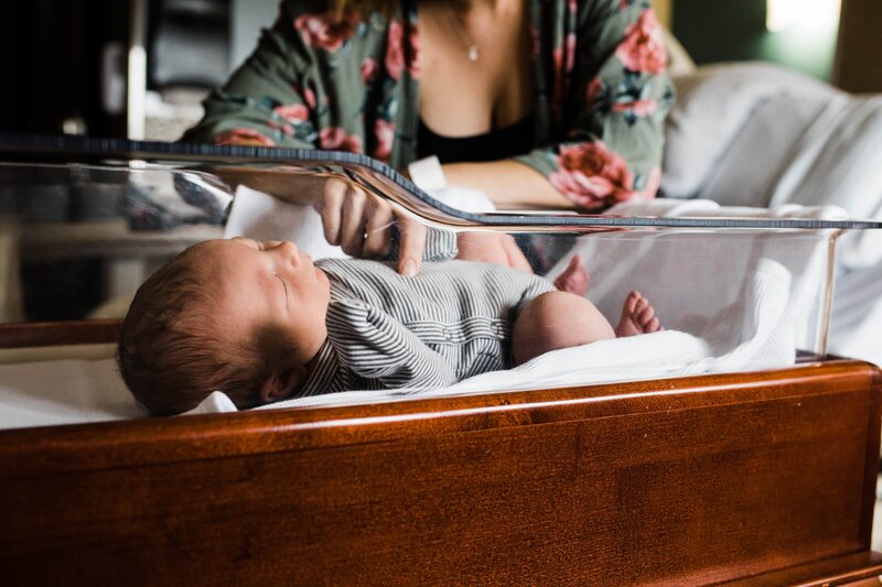 Newborn resting in a home bassinet while a parent looks on.