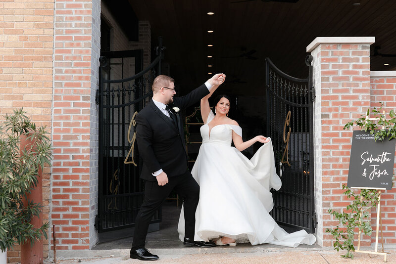 A bride and groom smiling as the groom twirls the bride outside the open wrought-iron gates of the Grbic events, a luxury wedding venue in st. louis