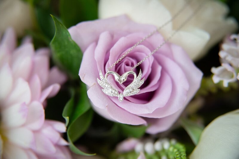 silver swan heart necklace laying on purple rose