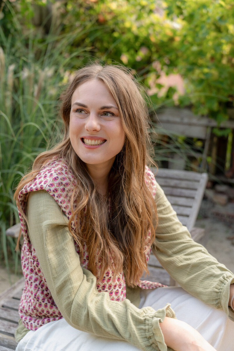 Patricia sitzt auf einer Bank und schaut lachend zur Seite.