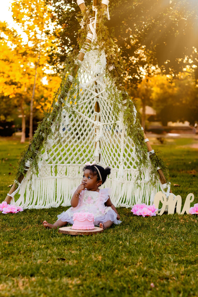 Cake Smash, a baby sit outside with a teepee eating cake 