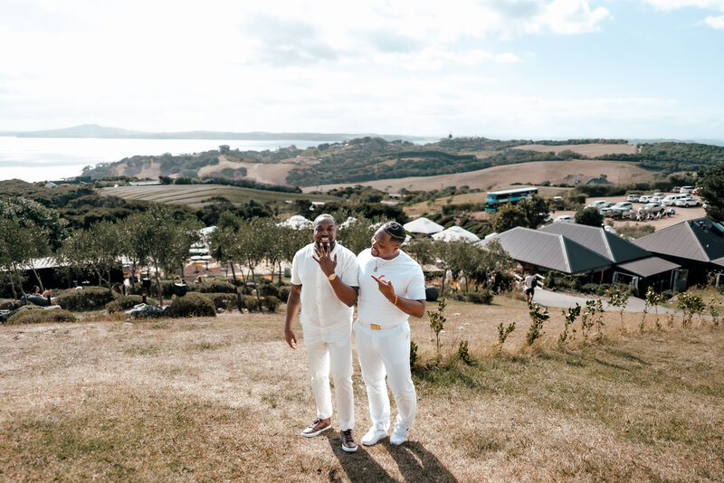 A LGBTQ couple standing next to each other on a clifftop at Mudbrick Vineyard being excited about their engagement - Zanthe Vorsatz Photography