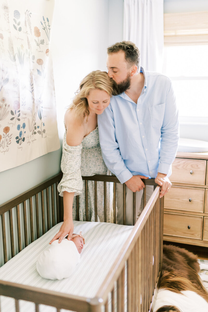 new mom kisses her baby girl on the top of her head in  her nursery