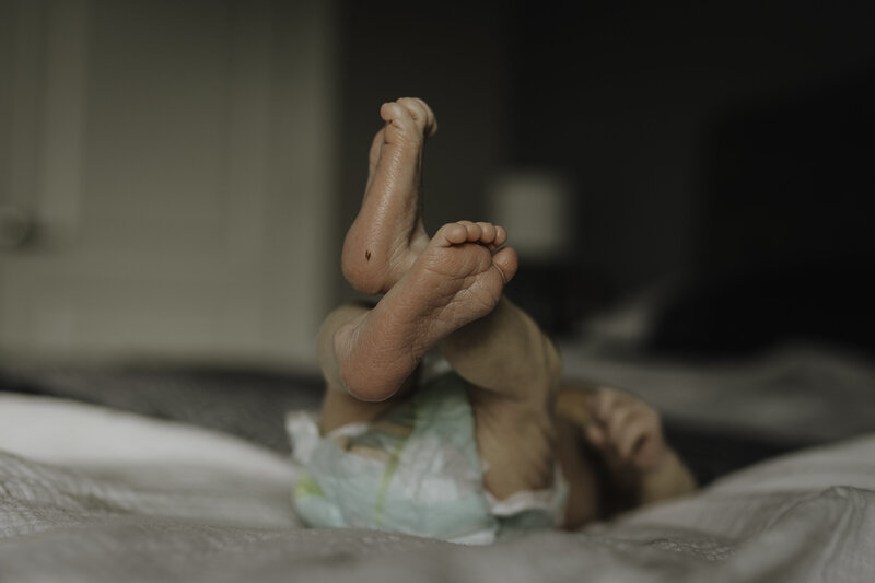 Verona B Photography captures baby details of a newborn - a newborn laying on a bed in his diaper with a close up of his feet and adorable toes. 