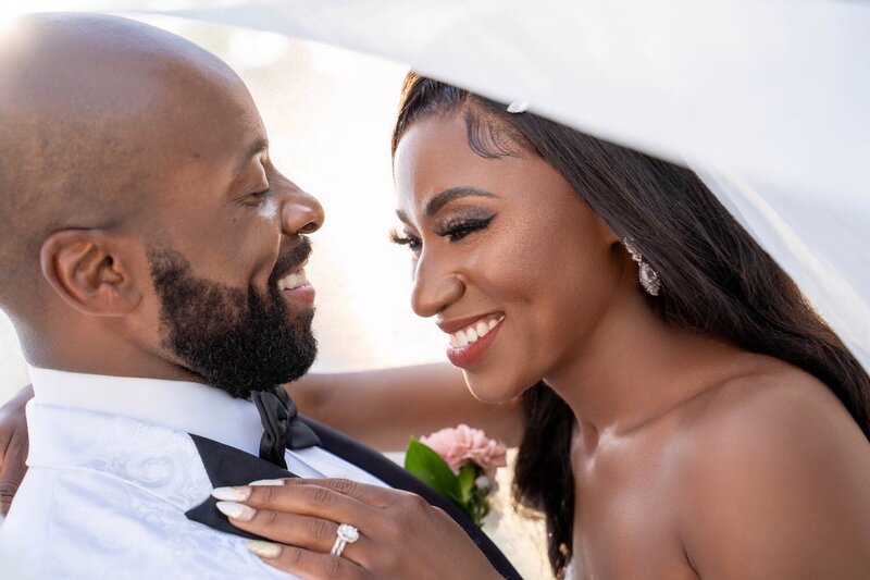 Bride and groom laugh joyfully under the veil in romantic close-up