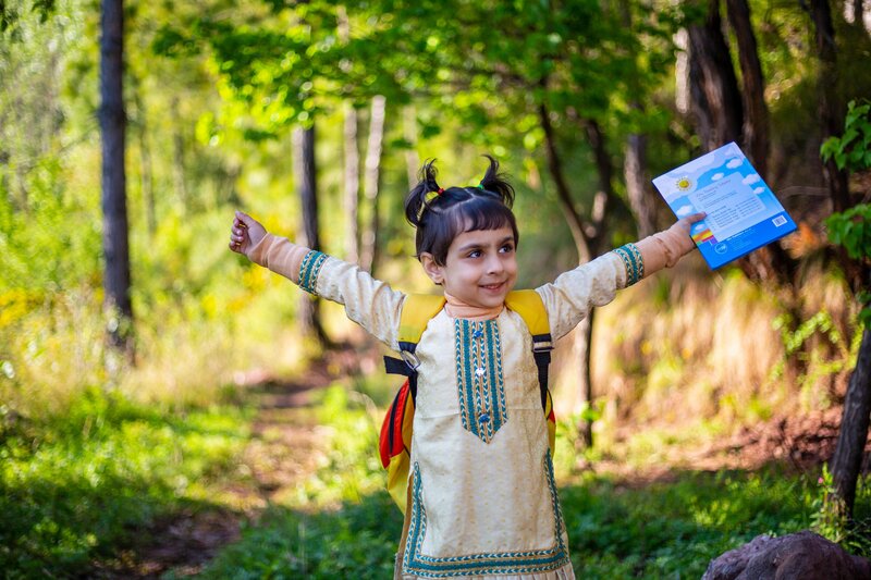 A young student with his hands up holding onto a book