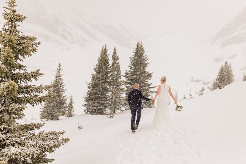 This captivating photograph captures a bride and groom walking hand in hand after landing by helicopter for a private ceremony in the Canadian Rockies. Surrounded by majestic mountain views, their intimate adventure wedding showcases the beauty of a secluded celebration in the Rockies, perfect for couples seeking an unforgettable, scenic experience.