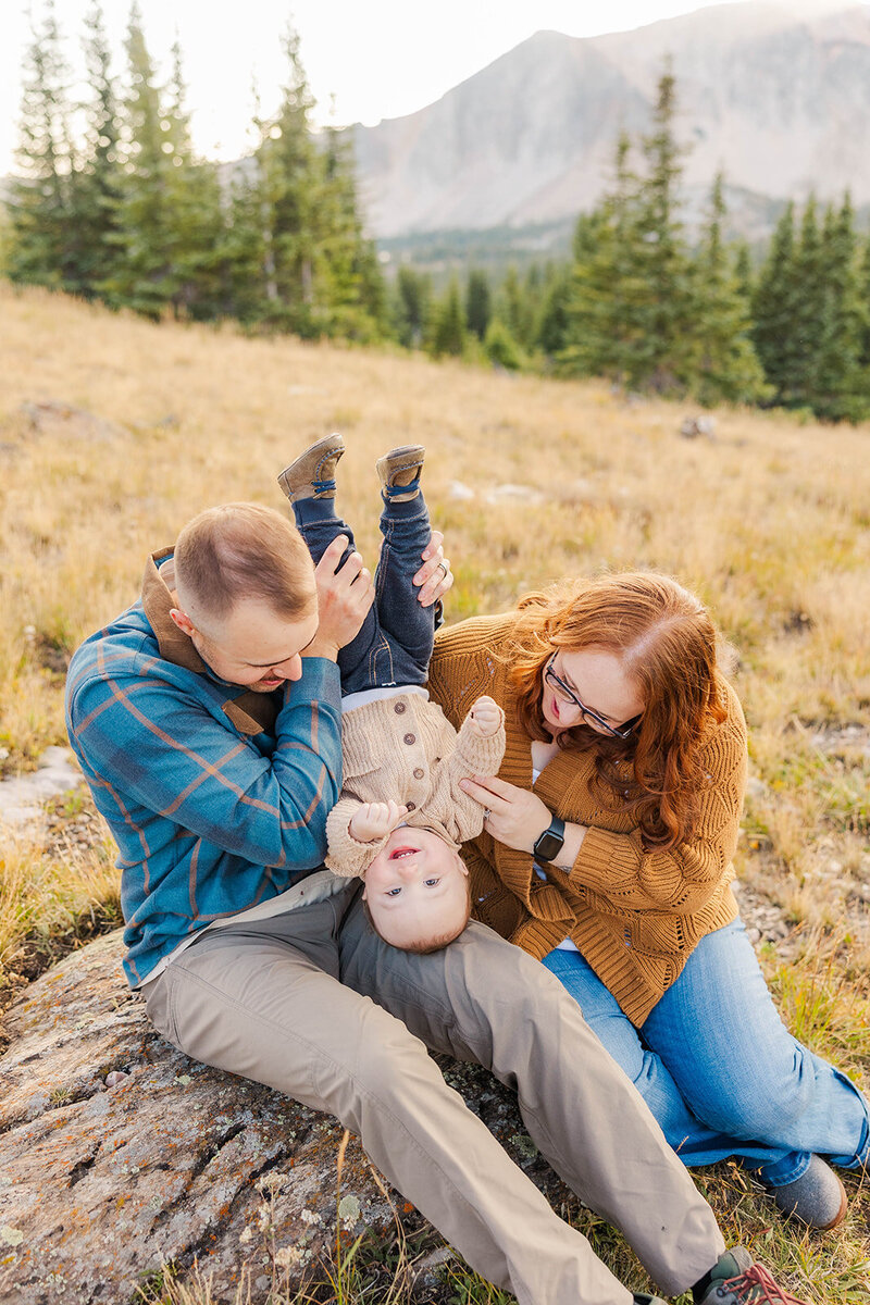 Family of 3 joyfully posing together on a rock at their family session in the Snowy Range Mountains near Laramie, Wyoming. 