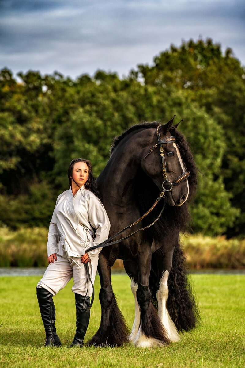 Female equestrian poses with a black Gypsy Vanner horse.