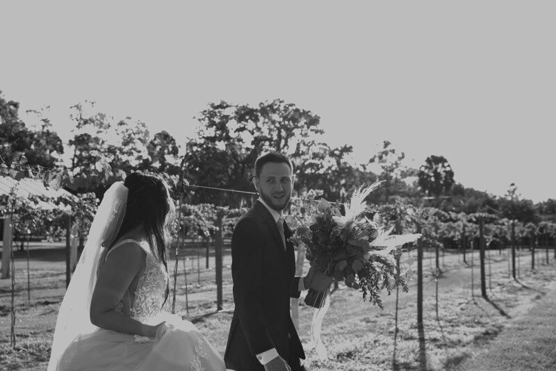groom holding bouquet and walking with bride in orlando vineyard
