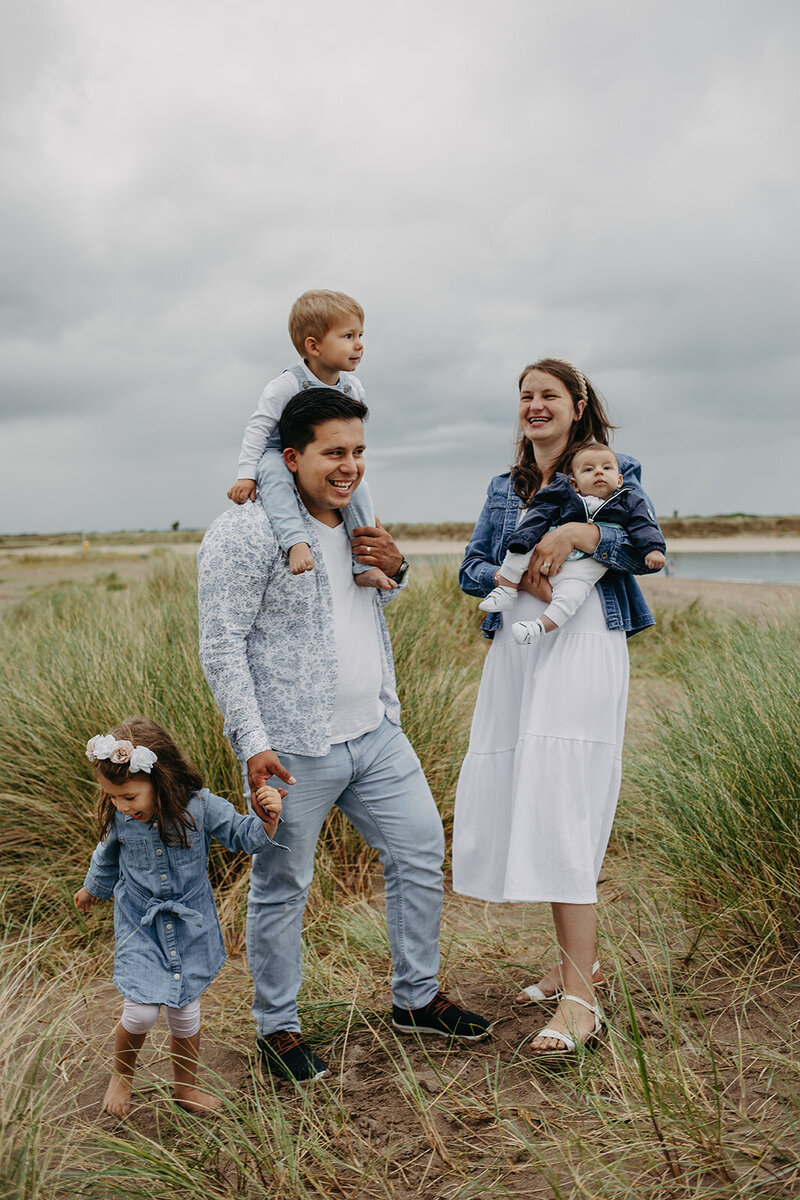 Candid family photo at the Malahide beach, with parents and three kids smiling and having fun in the sand , waves  and wild green grass 