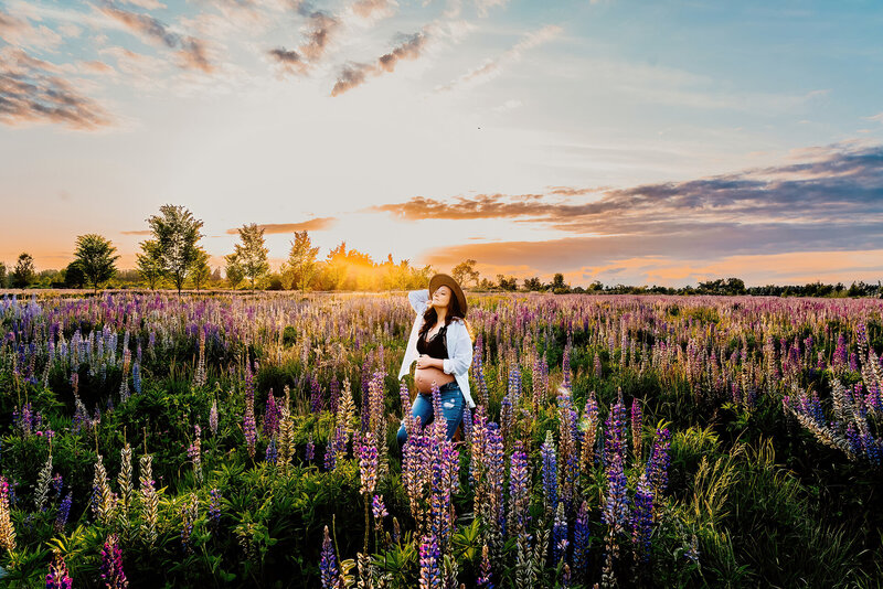 a pregnant mama in casual clothes sitting on a stool in a field of lupines in washington