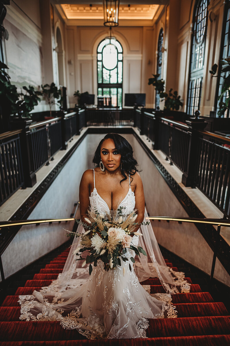 Maryland wedding photographer captures bride and a lace wedding dress standing at the top of a staircase that is adorned with red carpet and gold details for her Baltimore wedding