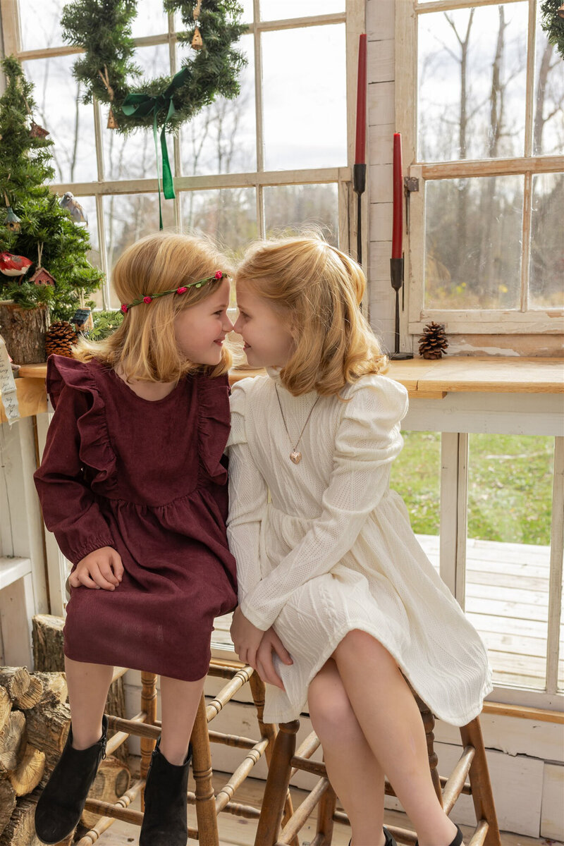 young sisters look at each other and touch noses while smiling at fern and pine greenhouse in dexter michigan