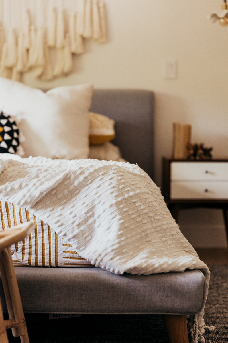 A nature inspired bedroom with textured blankets in focus and the bed and side table out of focus.