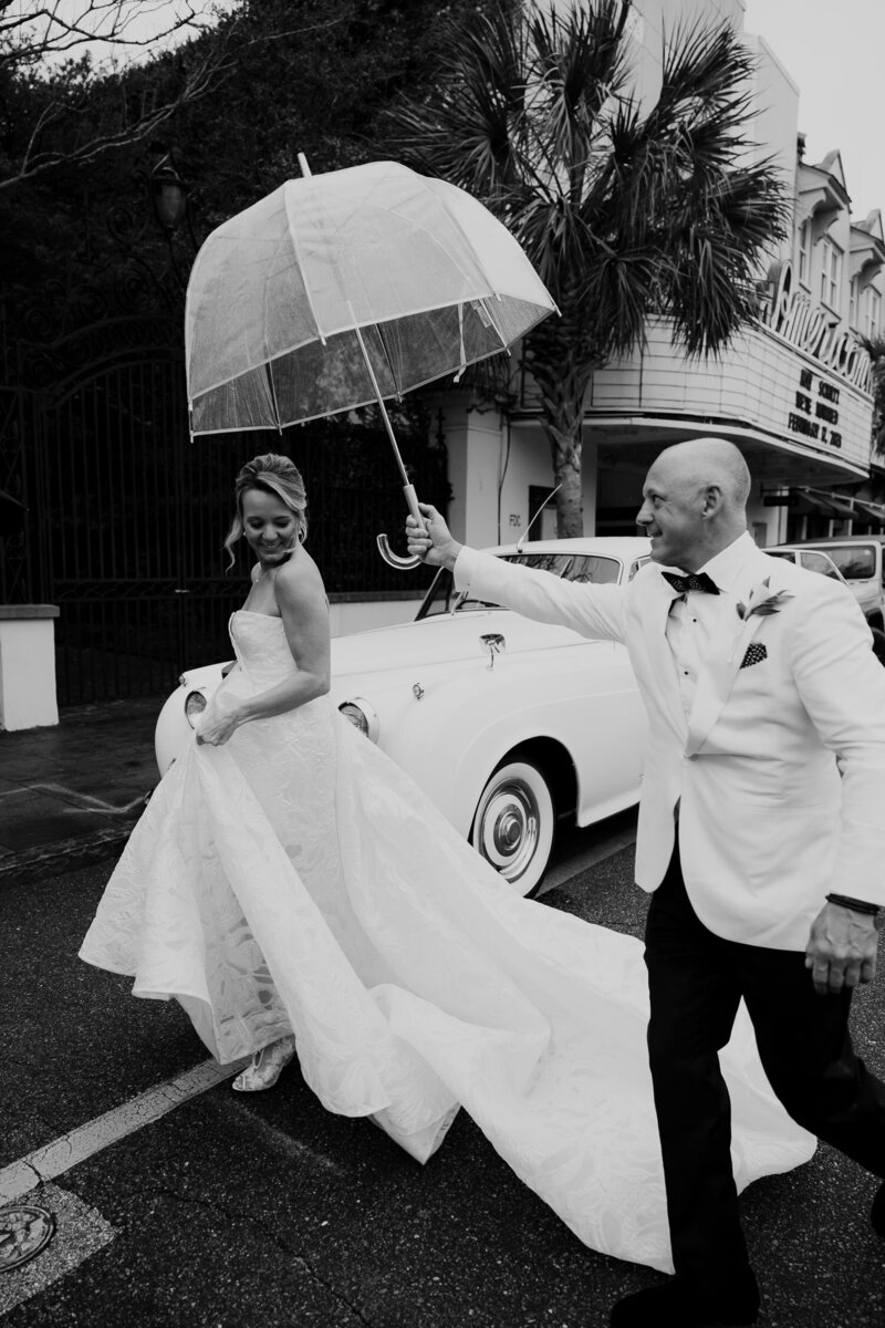 Charleston wedding with some rain. Groom holding a umbrella for his bride. Both walking in fron of the American Theatre and a Rolls Royce.