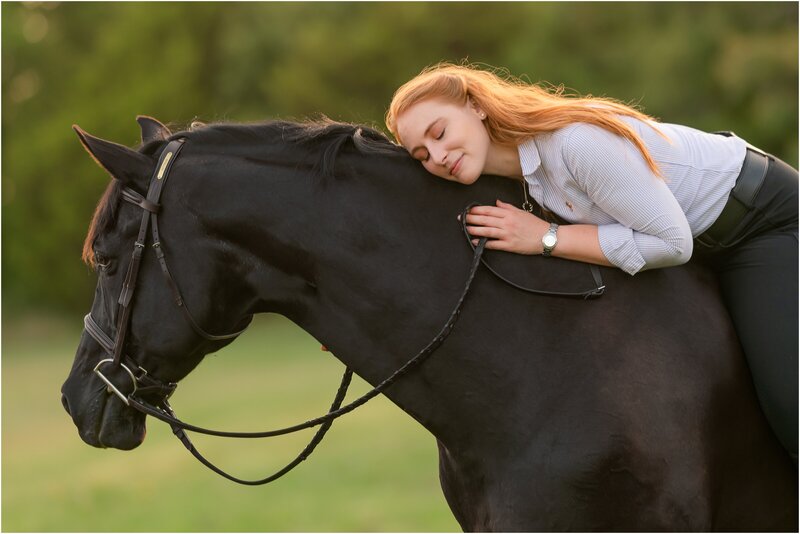 A red headed woman in black breeches sits bareback on her black gelding while leaning into his neck. They are photographed at their boarding barn in Stillwater Oklahoma