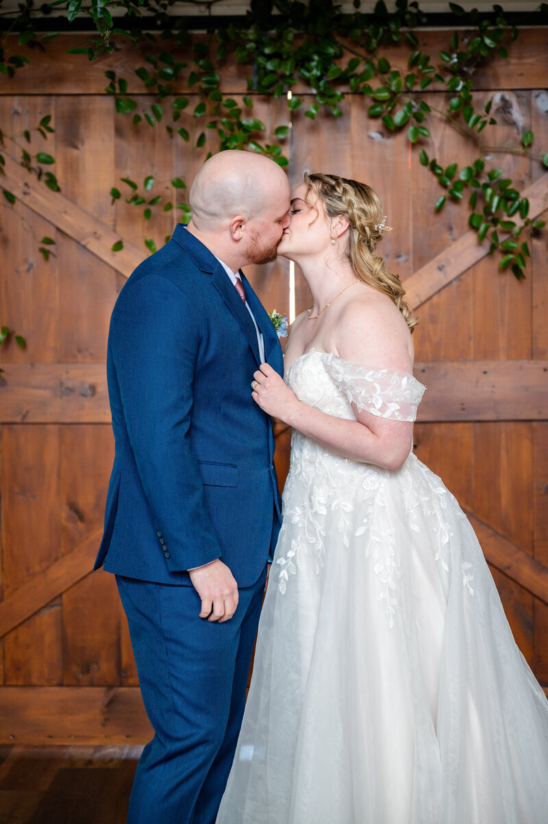 Wedding couple kisses in front of wooden barn doors in Northern VA wedding