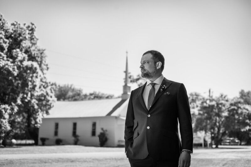 groom in front of small white church