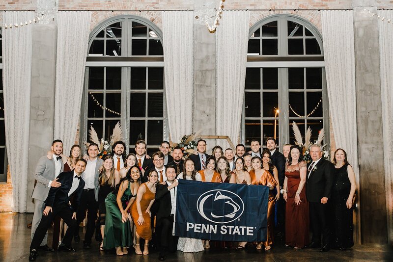 bride and groom holding a penn state flag with a large group of guests